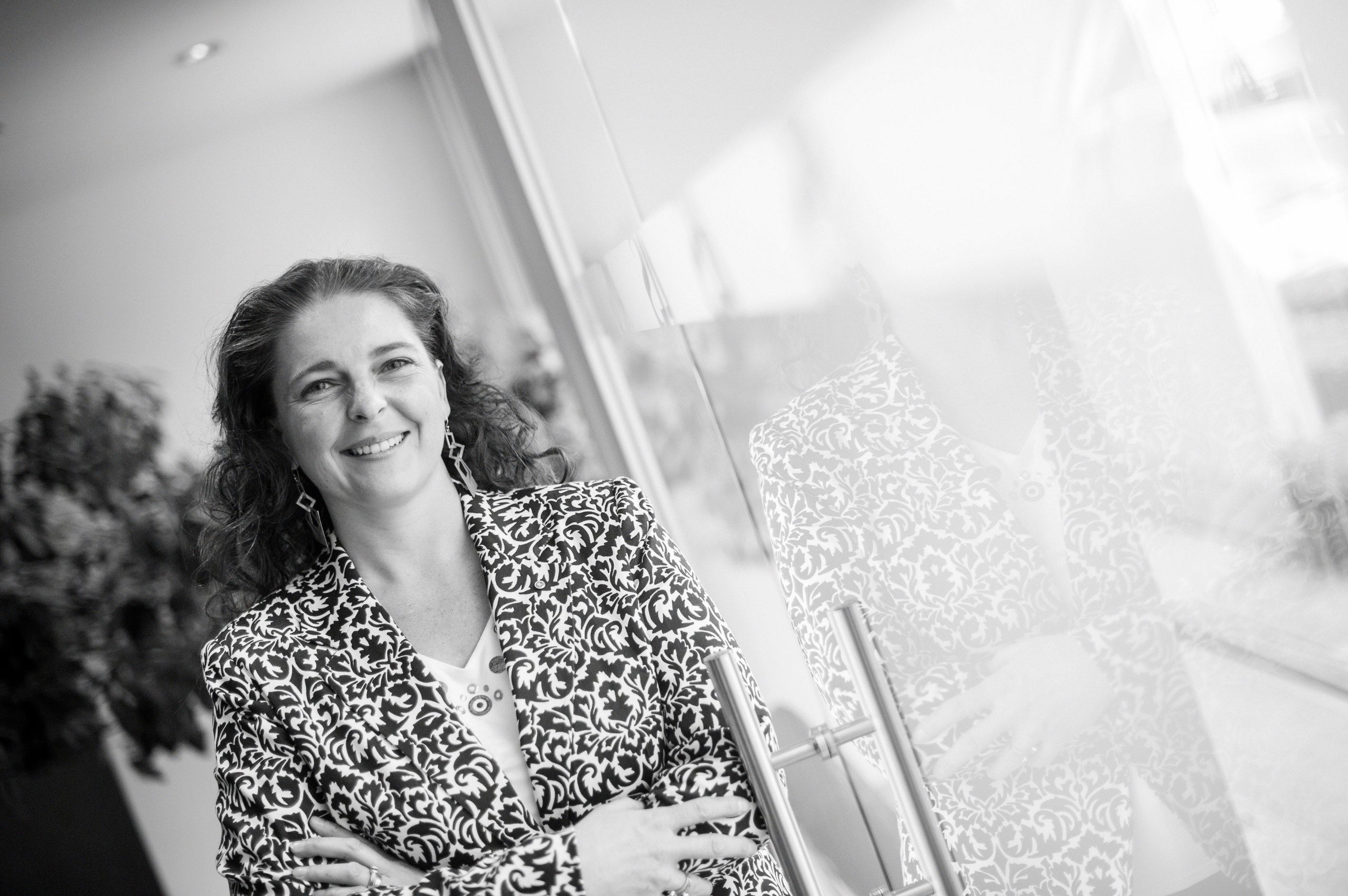Nathalie Frisch, souriante, bras croisés, adossée à une porte vitrée.